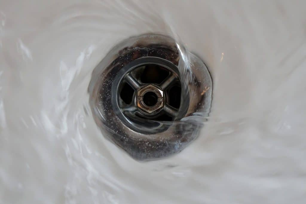 chemical drain cleaner product being carefully poured into sink drain with rubber gloves