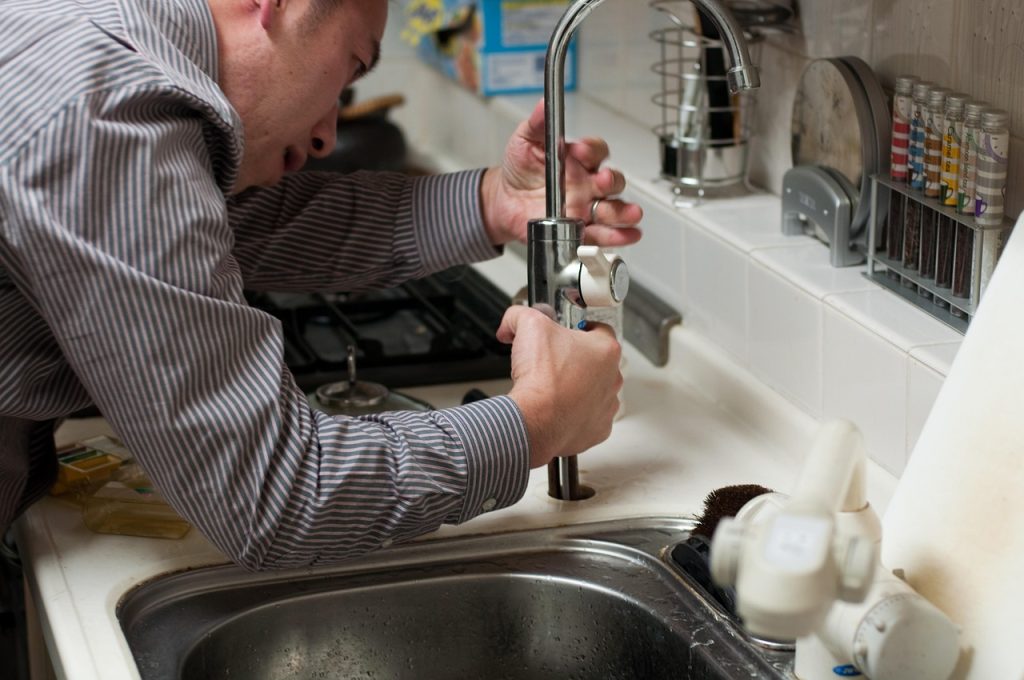 professional plumber inspecting under kitchen sink pipes