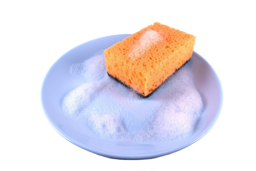 cleaning microwave turntable glass plate with sponge in sink