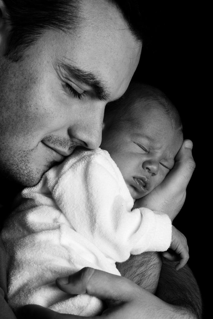 young Korean father holding baby while looking at financial documents at kitchen table